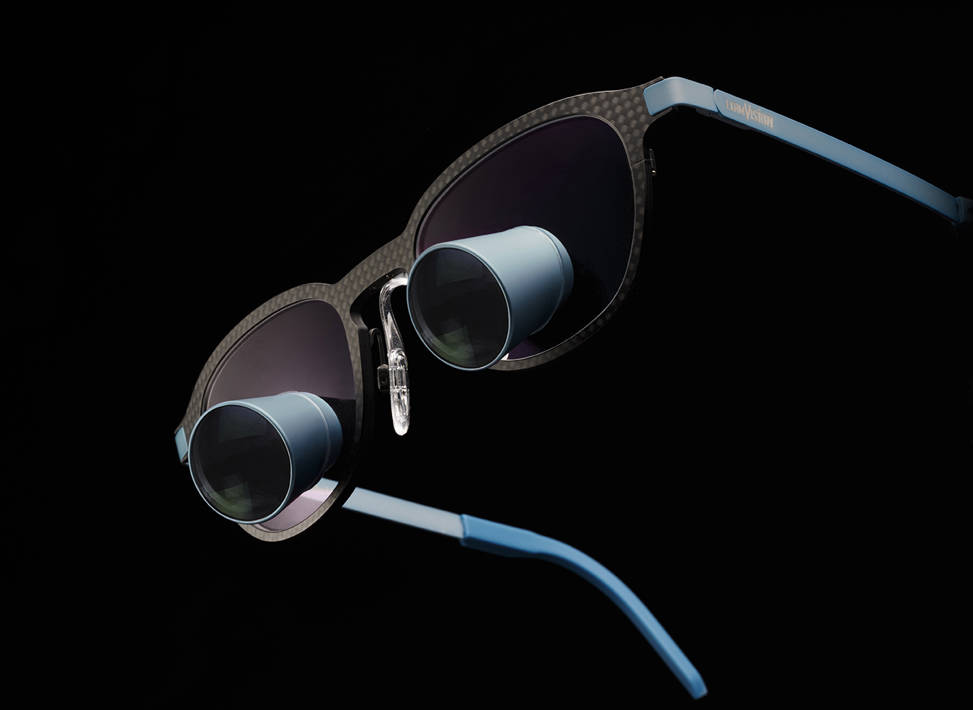 Galilean HD loupe by ExamVision in Carbon V2 frame with coloured oculars and temples in Blue Slate colour on a black background