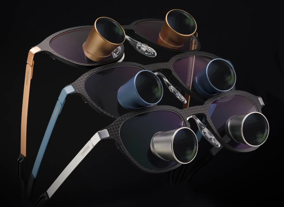 Three pairs of ExamVision loupes glasses in Carbon V2 frame with coloured oculars and temples on a black background
